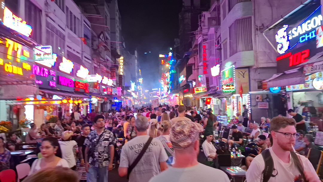 Night crowds in Saigon surrounded by glowing neon signs and busy open-air bars.