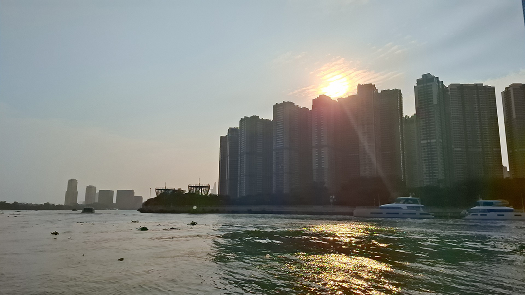 Sunset view over the Saigon River with tall city skyscrapers reflecting on the shimmering water.