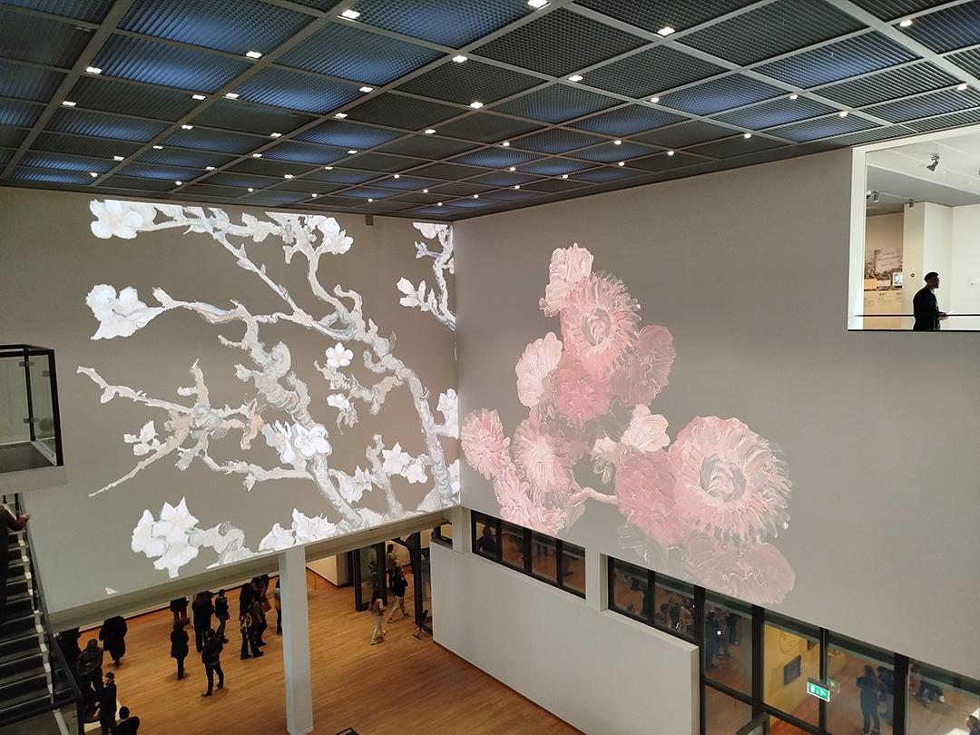 Interior of the Van Gogh Museum in Amsterdam with visitors and projected floral visuals inspired by the artist’s style.