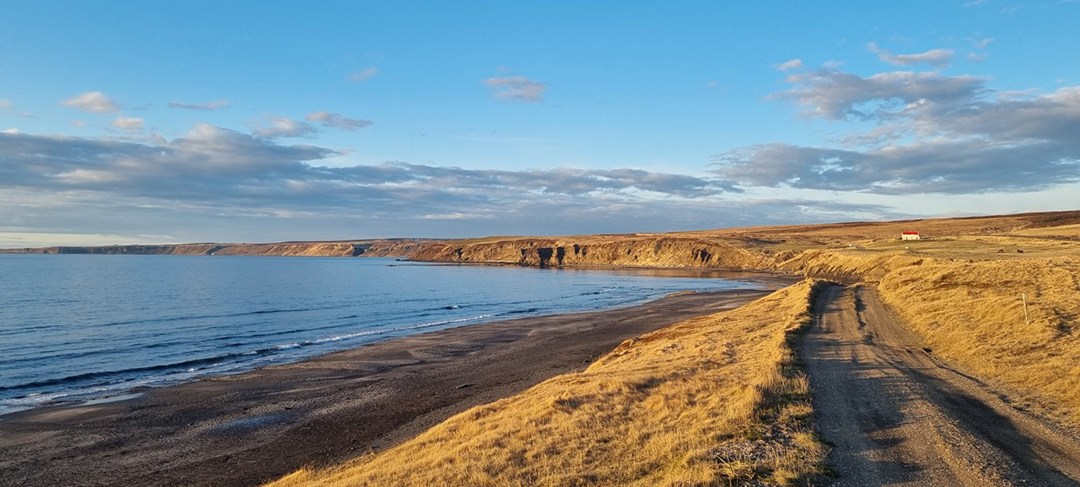 Obala pri mestu Húsavík na severu Islandije z razgledom na črno peščeno plažo, mirno morje in dramatično islandsko pokrajino ob severnem Atlantiku.