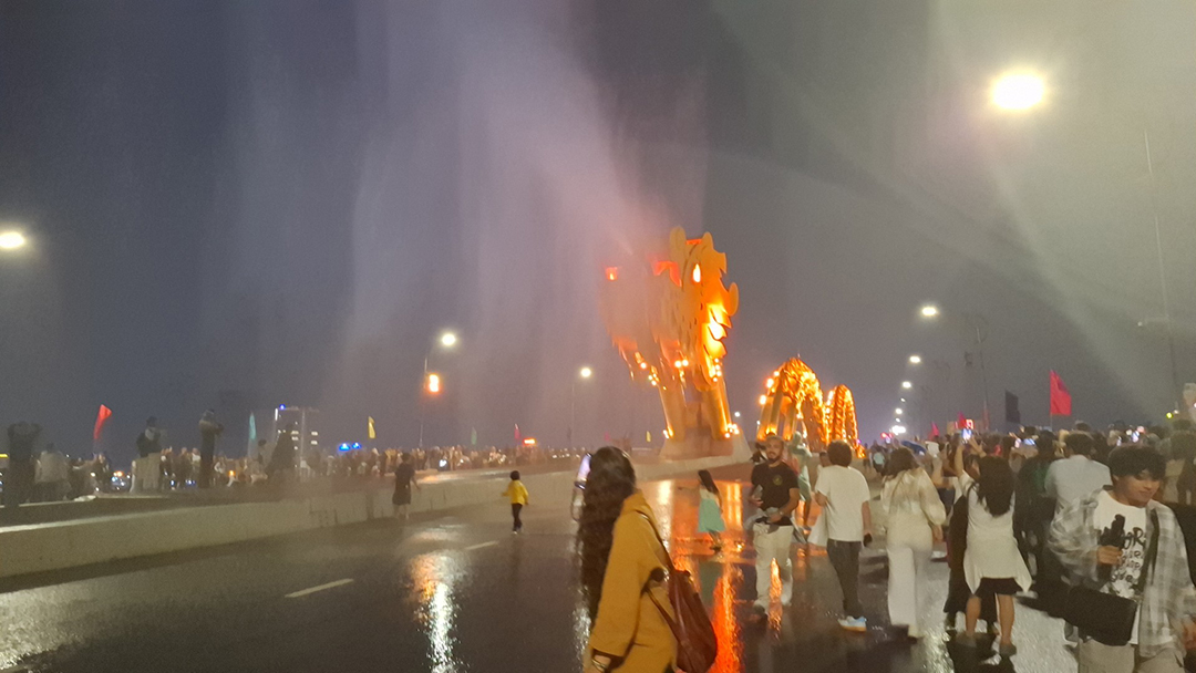 Zmajev most v Da Nangu v Vietnamu ponoči, osvetljen most z množico ljudi med večernim spektaklom ognja in vode.