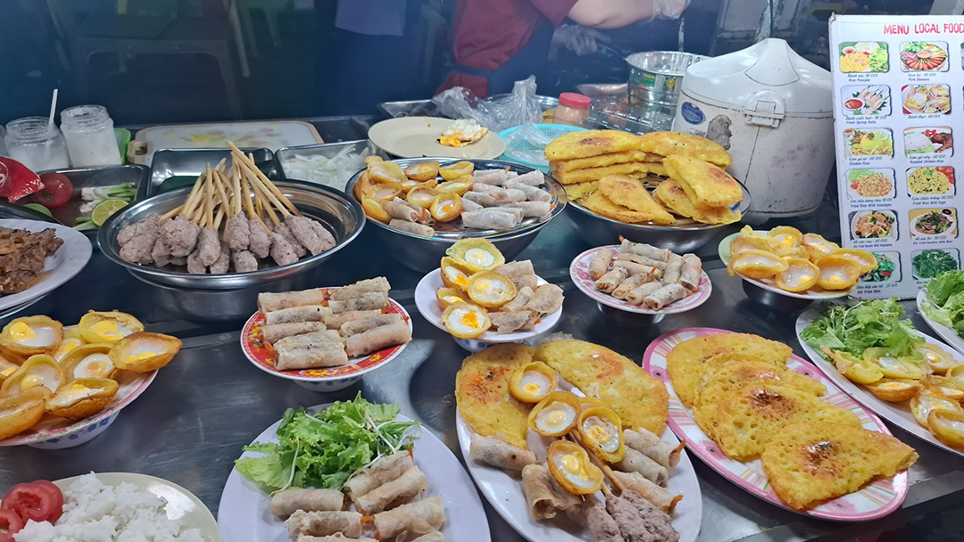 Različne tradicionalne vietnamske jedi na ulični stojnici, vključno s spomladanskimi zavitki, jajčnimi jedmi in riževimi specialitetami.