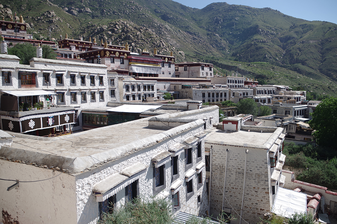 Pogled na bele stavbe samostanskega kompleksa Drepung, ki se razprostira po gorskem pobočju nad Lhaso.